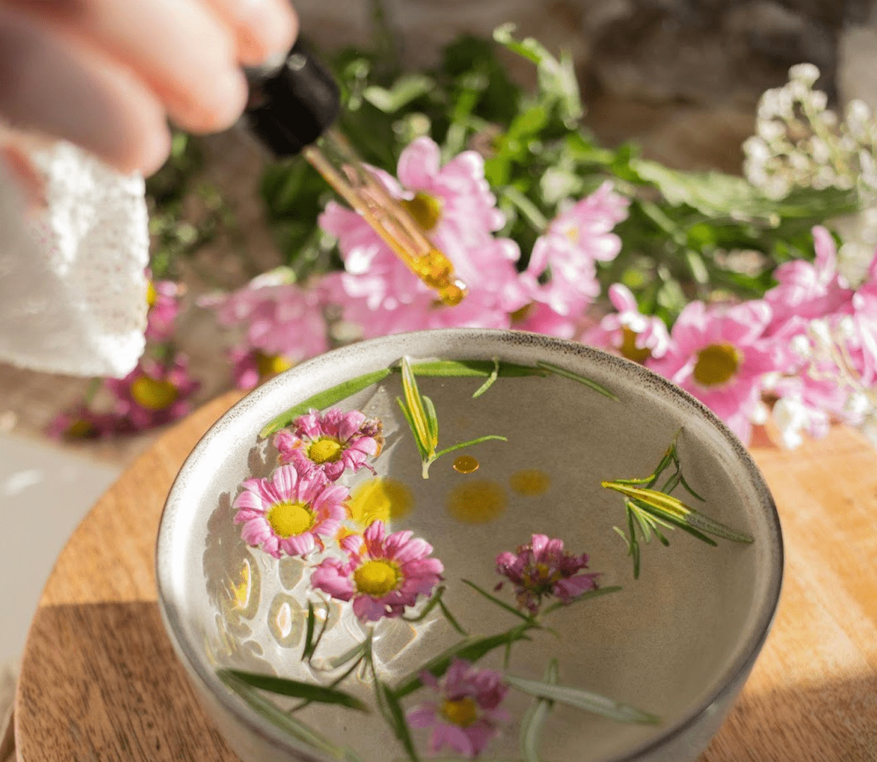 A woman drops a few drops of Dragon’s Blood oil into a bowl of water with other botanicals