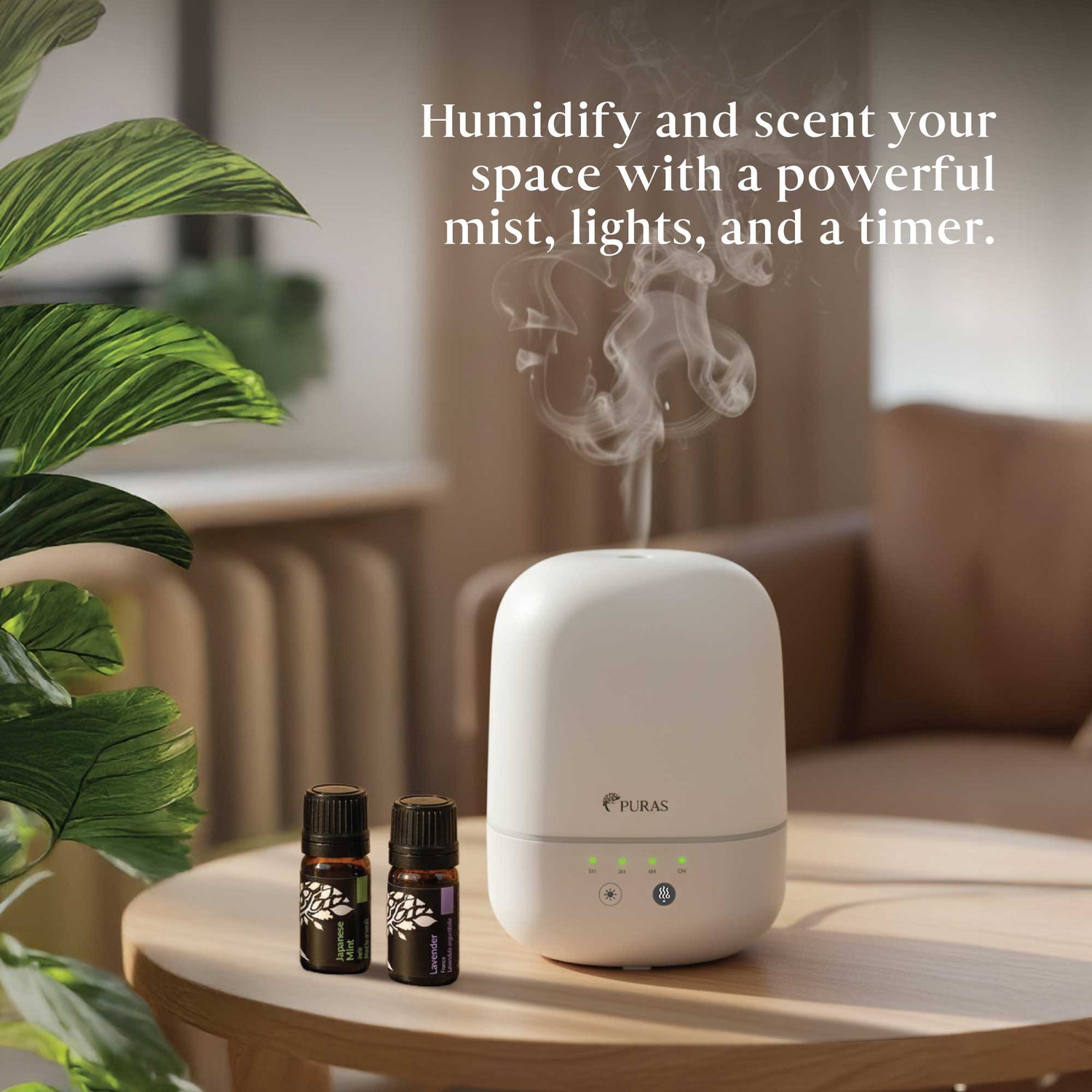 A white PURAS humidifier and diffuser sits on a light wood table in a cozy living room setting, with mist rising from the top. Two small essential oil bottles are placed beside it, and a large green plant leaf is visible on the left.