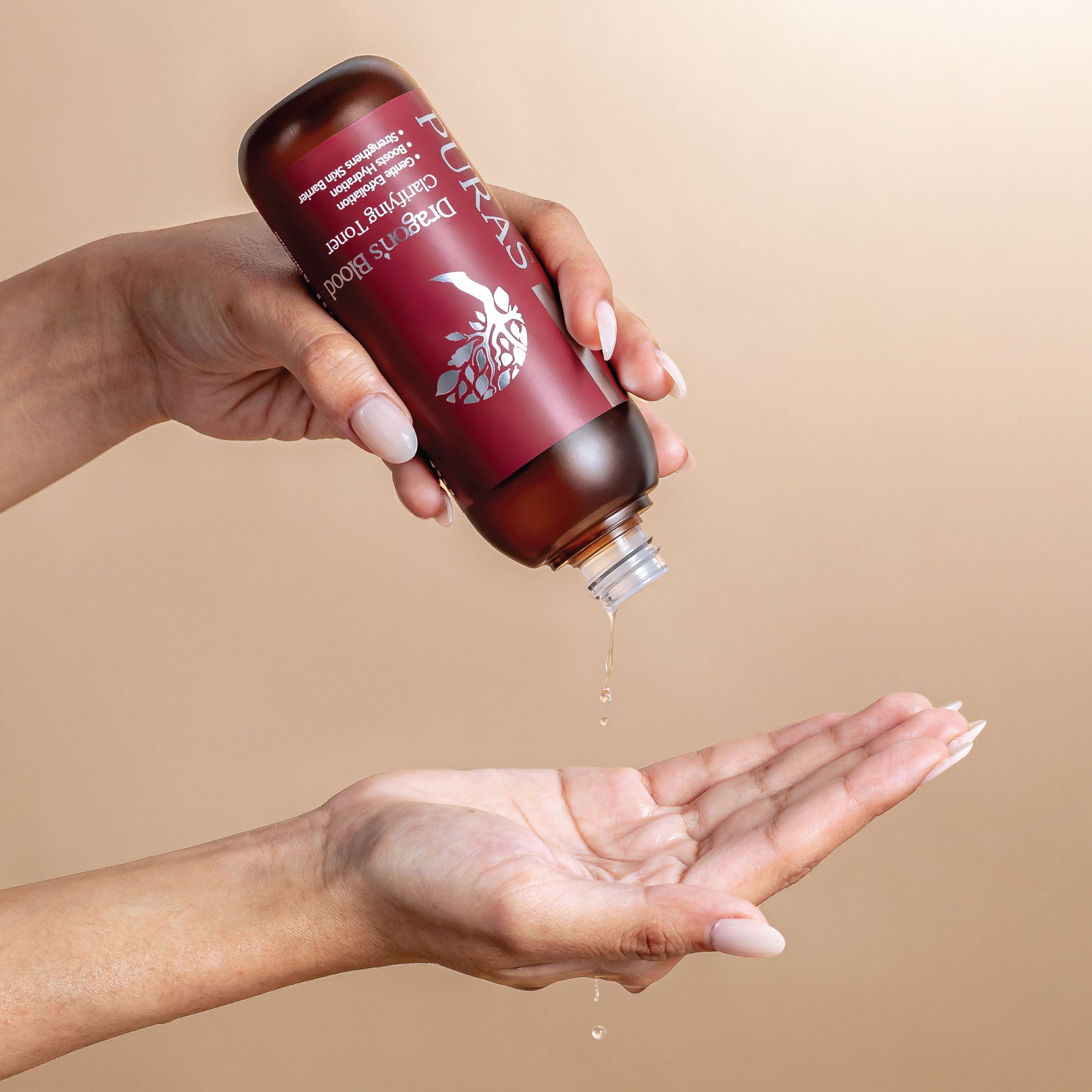 Hand holding a Puras Dragon's Blood Clarifying Toner with a label, pouring liquid into another hand against a beige background
