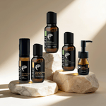 Five PURAS skincare bottles arranged on stacked stone slabs against a warm beige background with soft sunlight and shadows. The products include copper-rich face wash, copper-rich body wash, eye cream, and serum in amber glass and black packaging.