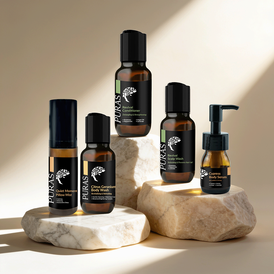 Five PURAS skincare bottles arranged on stacked stone slabs against a warm beige background with soft sunlight and shadows. The products include copper-rich face wash, copper-rich body wash, eye cream, and serum in amber glass and black packaging.