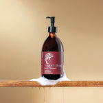 Bottle of 'Dragon's Blood' body cleanser with a pump with texture on a wooden surface against a beige background