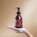 Bottle of Puras Dragon's Blood Face Wash with a hand holding foam on a beige background