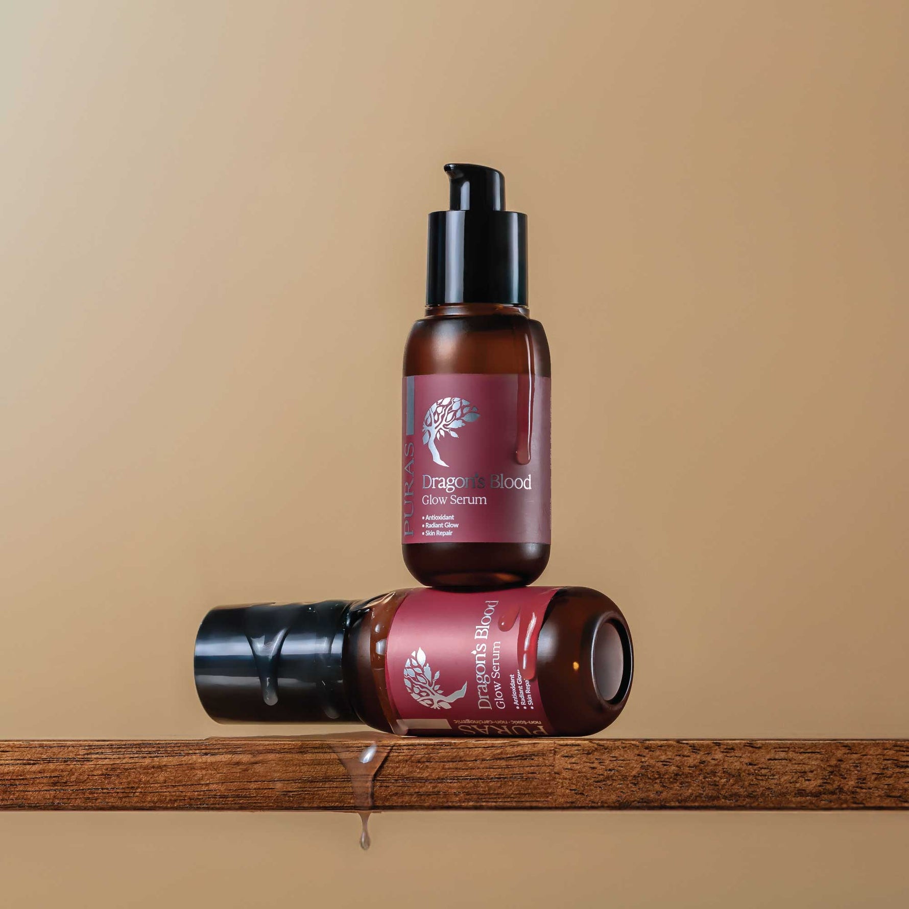 Two bottles of Dragon's Blood serum flowing down the bottle on a wooden surface with a beige background
