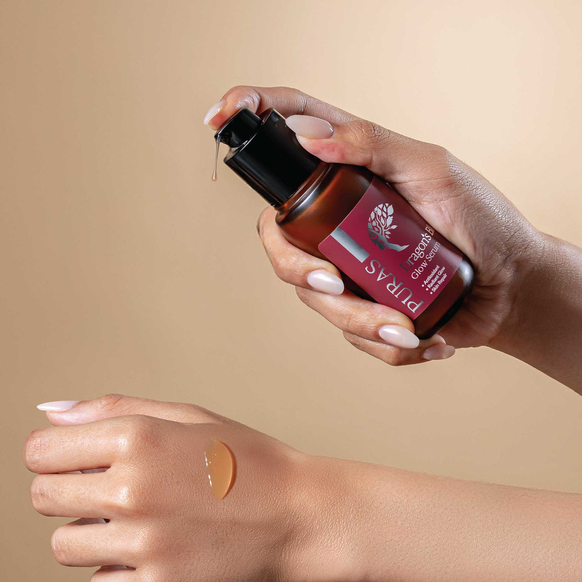 Hand holding a bottle of Puras Glow Serum product with the serum texture on a hand in a beige background