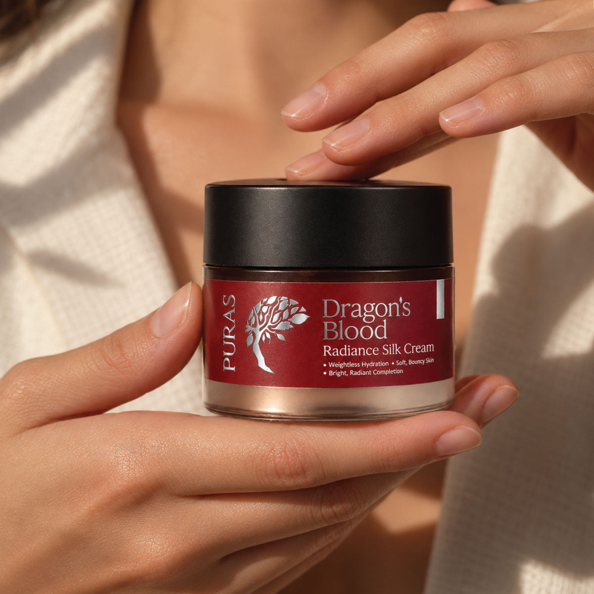 PURAS Dragon’s Blood Radiance Silk Cream held gently in warm natural light.