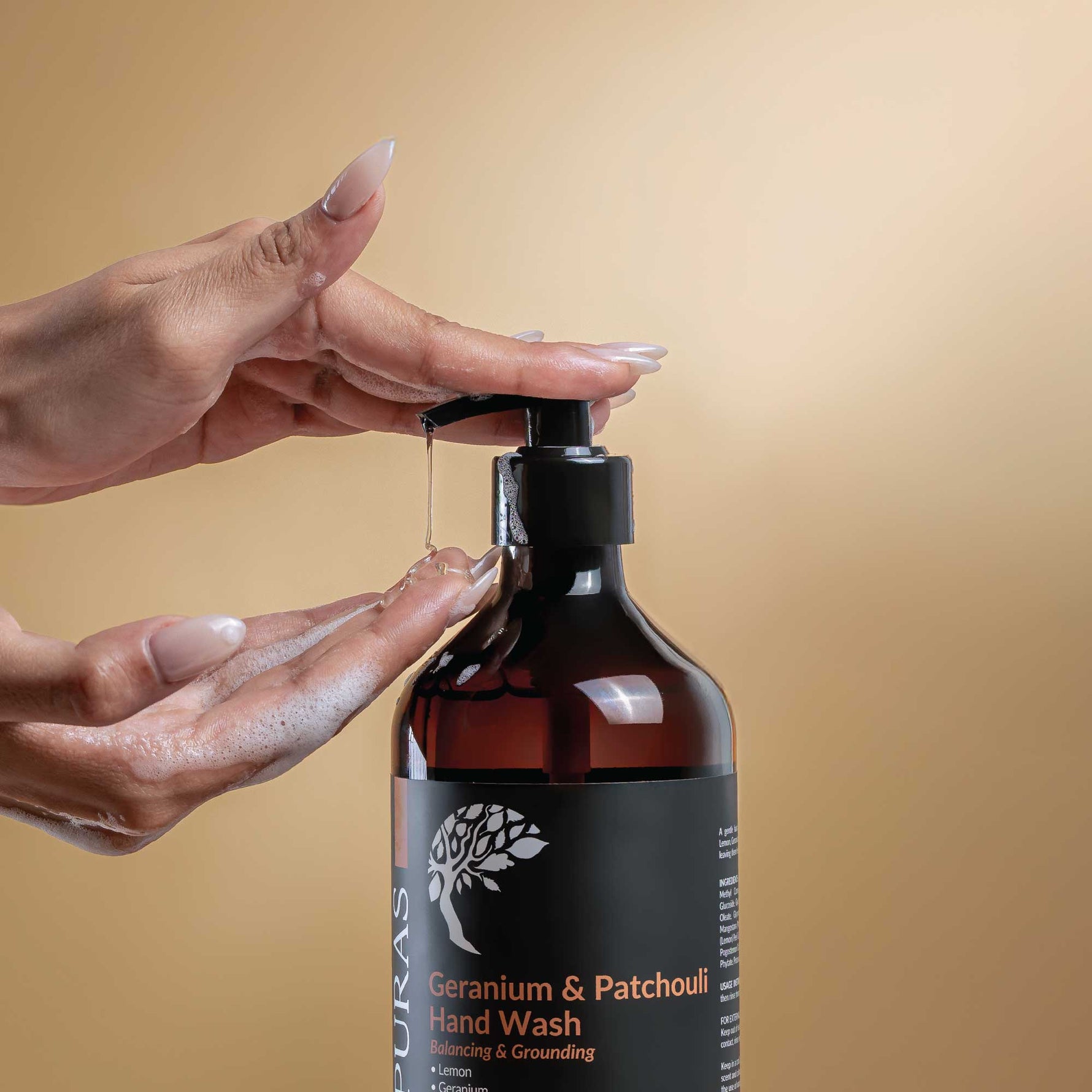 Hand holding a pump of Puras Geranium & Patchouli Hand Wash against a beige background