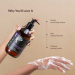 Puras lavender body wash bottle with a hand holding it and another hand with soap suds on a beige background.