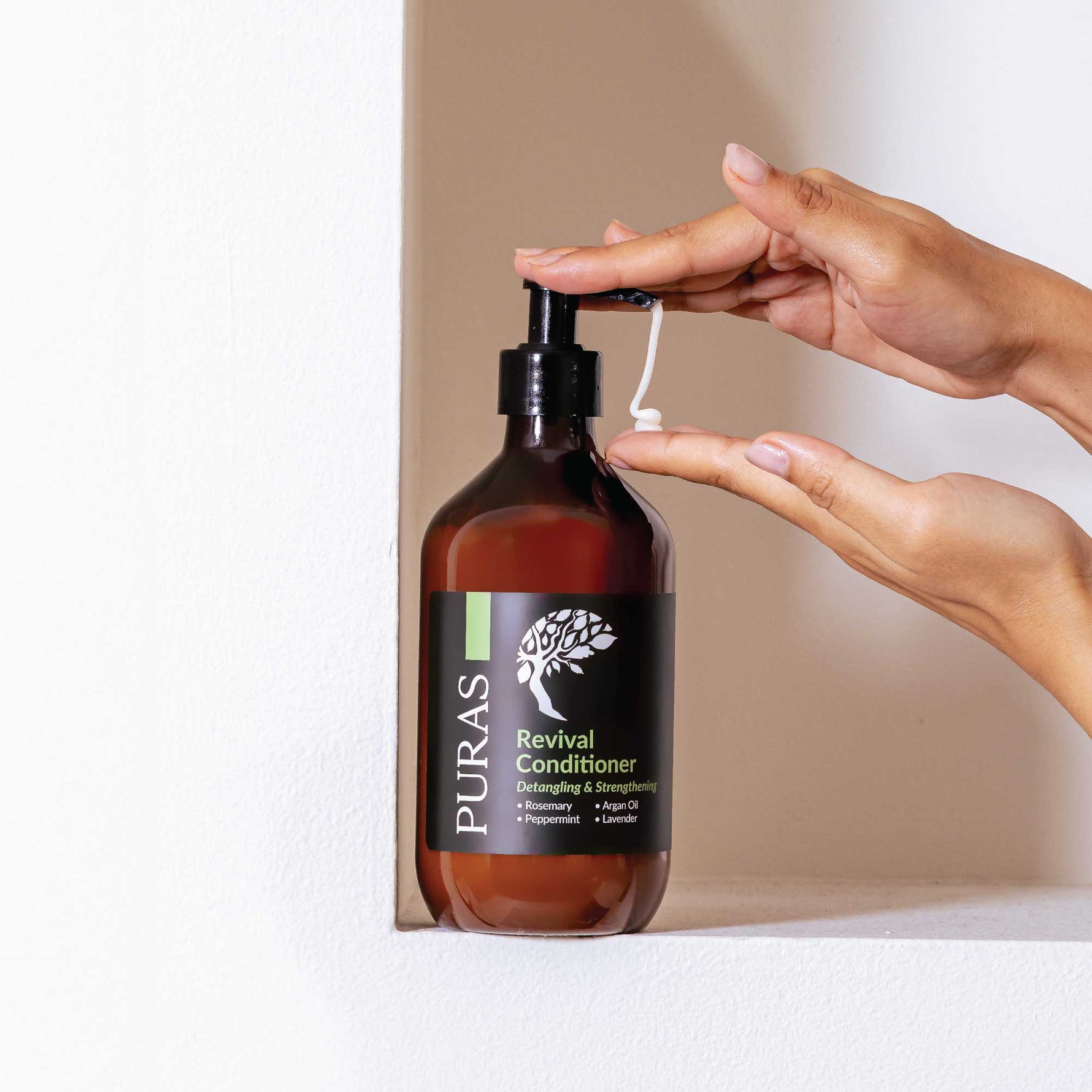 Hand holding a bottle of Puras Revival Conditioner with a pump.